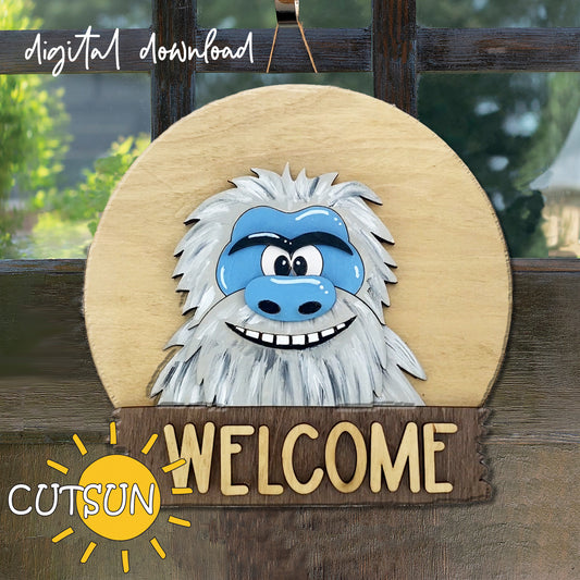 A digital illustration of a round door hanger sign featuring a cartoonish character resembling a Yeti or Bigfoot with the text 'WELCOME' on a wooden background. The sign also has a slot for seasonal add-ons.