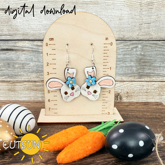 A digital download for Easter Bunny Earring designs displayed alongside carrots and an egg, indicating the design theme. The image shows a wooden board with a ruler for scale.