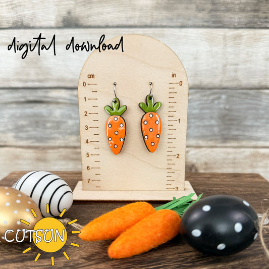 A digital rendering of carrot-shaped dangle earrings with polka dots and leafy greens, displayed next to a wooden ruler for scale, on a background featuring carrots and Easter eggs.