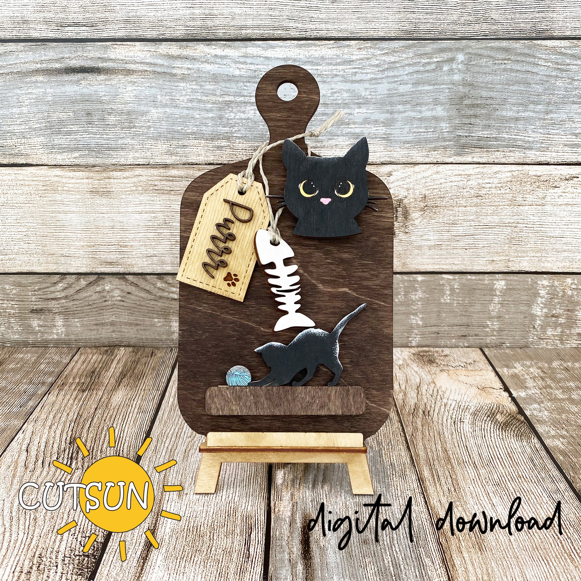 A digital image showing a wooden cutting board decoration with a cat face, a tag with a paw print, and a kitten playing with a ball of wool, marked with the word 'Purr'.