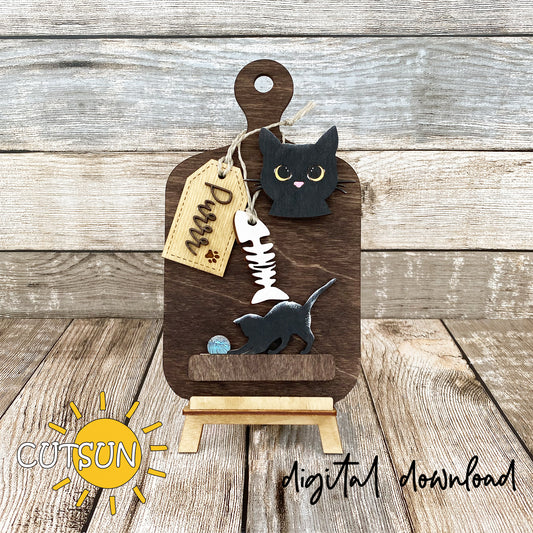 A digital image showing a wooden cutting board decoration with a cat face, a tag with a paw print, and a kitten playing with a ball of wool, marked with the word 'Purr'.