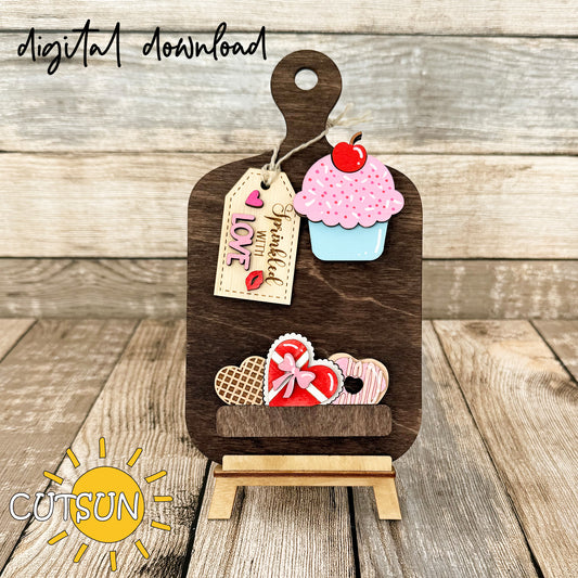 A digital download image showing a wooden cutting board decorated with a cupcake, heart-shaped waffle, box of chocolates, and a doughnut, adorned with love-themed tags.