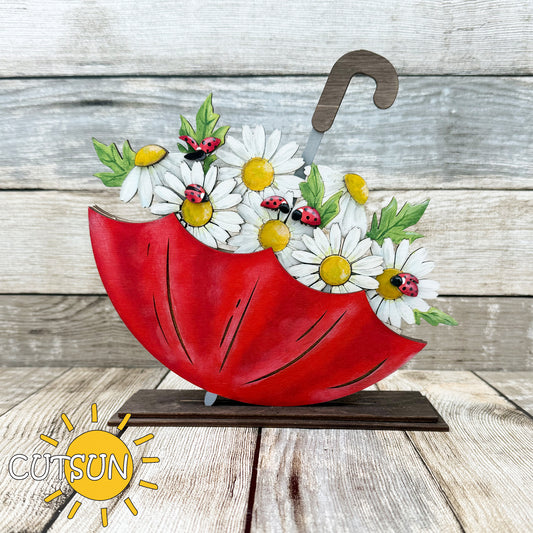 A digital image showing a red umbrella-shaped shelf sitter with white daisies and ladybugs designed for laser cutting.