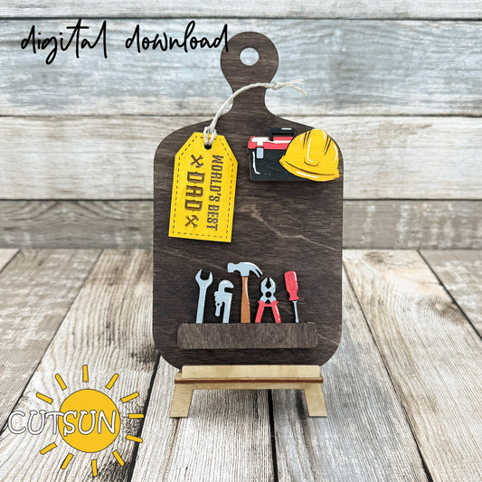A digital rendering of a laser-cut wooden cutting board decor with interchangeable tools and a 'World's Best Dad' tag, displayed on a wooden stand.