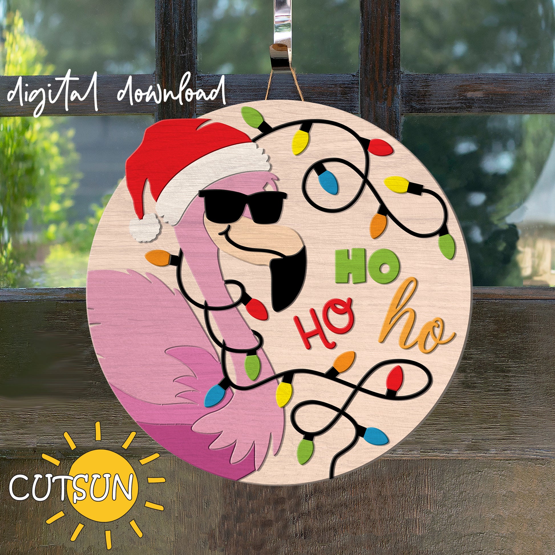 Decorative sign with flamingo wearing a Santa hat and sunglasses, surrounded by Christmas lights, on a wooden surface.