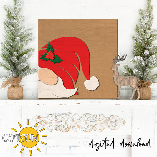 Wooden cutout of a red Santa hat with holly leaves on a white surface with Christmas decor.