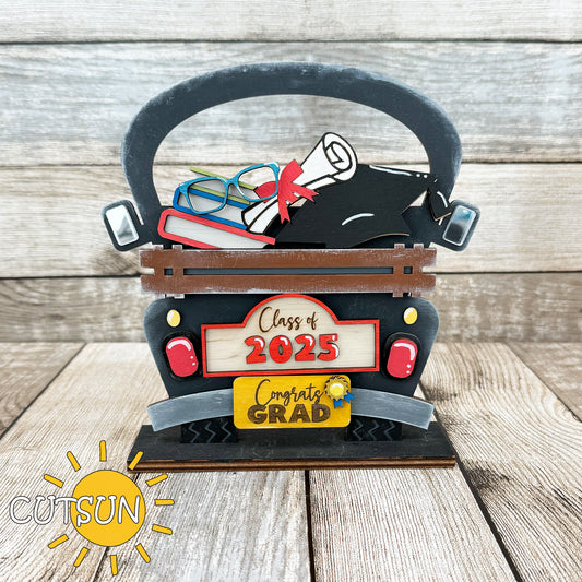 A laser cut file depicting a graduation-themed add-on for an interchangeable farmhouse truck, featuring elements like a pile of books, eyeglasses, a diploma, a graduation cap, a plaque with 'Class of 2025', and a license plate with 'Congrats GRAD'.