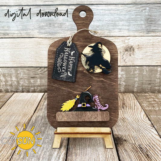 A digital download for a laser cut file featuring a wooden cutting board with Halloween-themed decorations including a witch, a broom, a witch's shoe, a witch's hat, and a 'Happy Halloween' tag.
