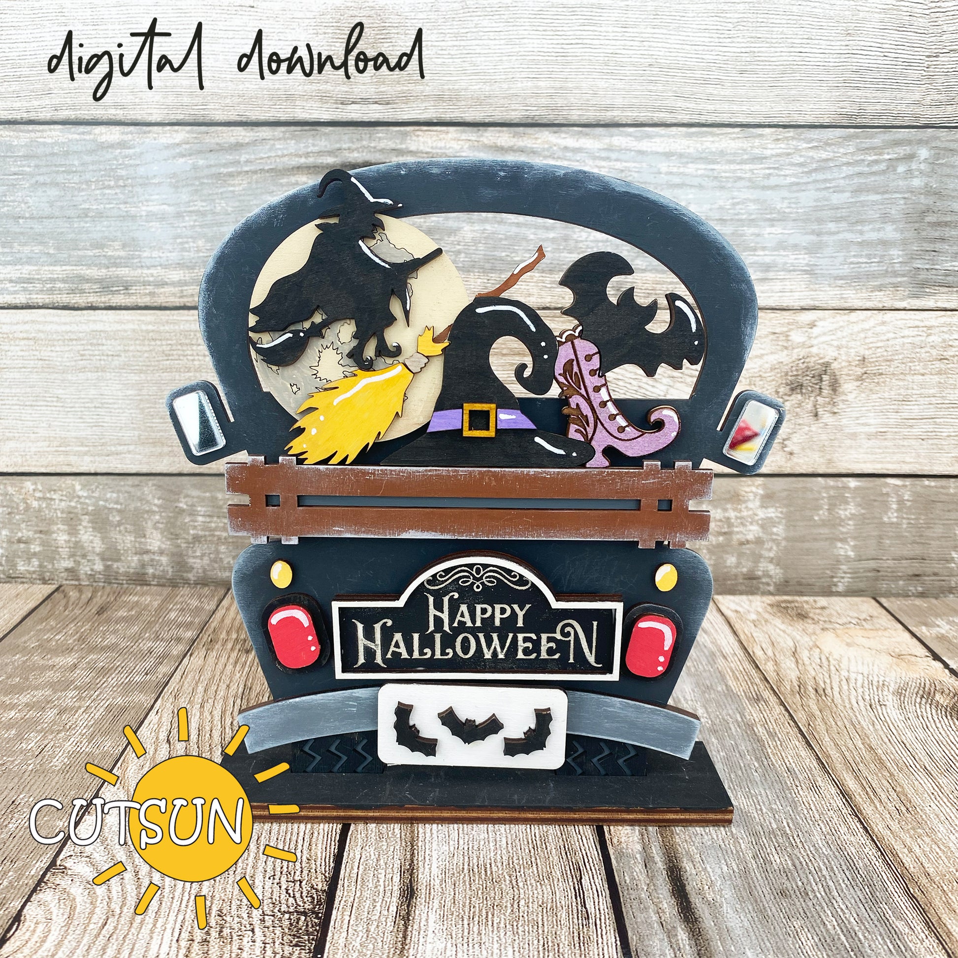A decorative truck-shaped sign with a 'Happy Halloween' message, featuring silhouettes of a witch, a broom, a hat, a bat, and a shoe, and Halloween-themed embellishments.