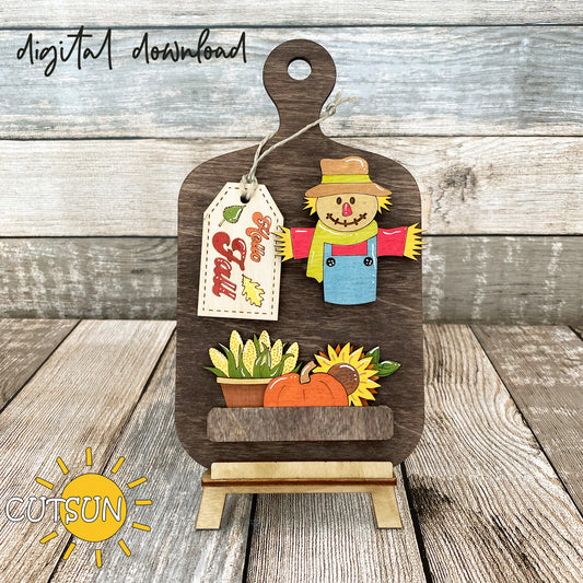 A digital download image showing a wooden cutting board decoration with a scarecrow, pumpkin, sunflower, and a 'Hello Fall' tag.