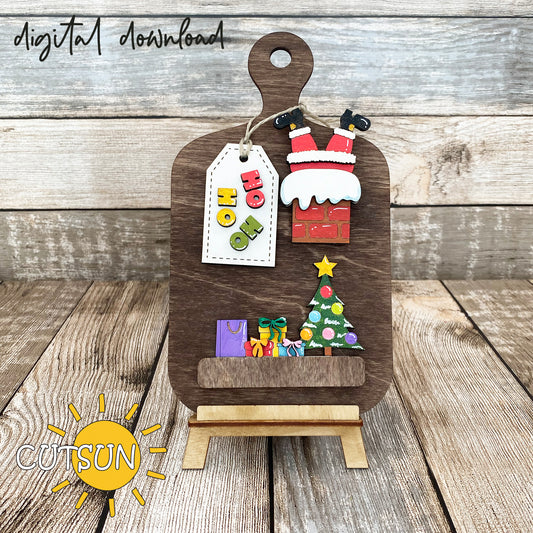 A digital download image showing a wooden cutting board with a Christmas themed decoration, including Santa, a Christmas tree, and gifts.