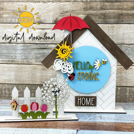 A digital download image showing a laser cut file decoration for a house and fence shelf, featuring elements like a birdhouse, umbrella, and floral designs, with the text 'Hello Spring' and 'Home'.