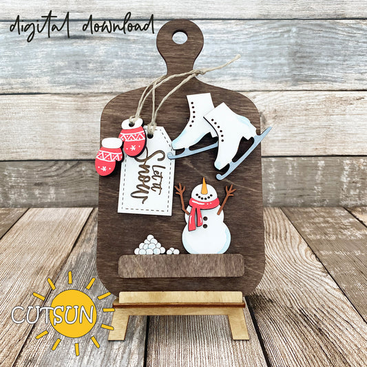 Digital download for a faux cutting board shelf sitter featuring ice skates, mittens, a snowman, a pile of snowballs and a tag with the text 'Let it Snow'.