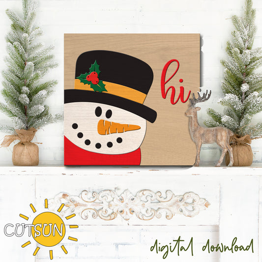 Decorative sign with a snowman design and 'hi' text, surrounded by Christmas decor on a white wooden surface.
