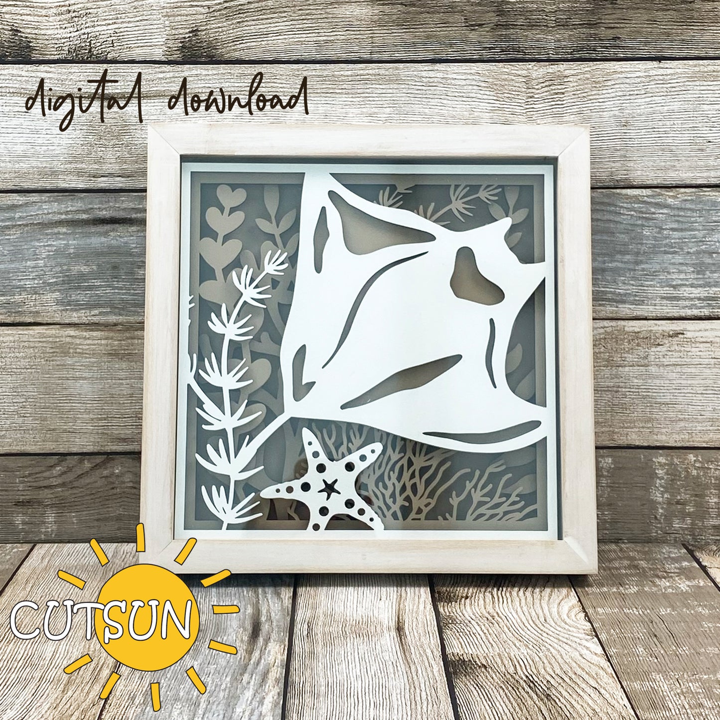 Layered shadow box design featuring a manta ray swimming among coral, seaweed, and a starfish, displayed in a wood frame.