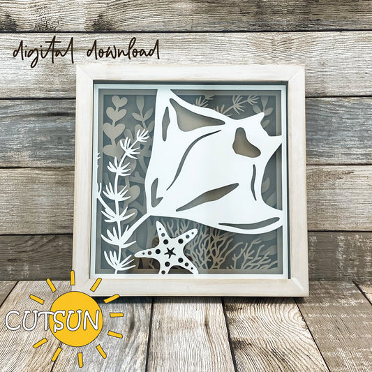 Layered shadow box design featuring a manta ray swimming among coral, seaweed, and a starfish, displayed in a wood frame.