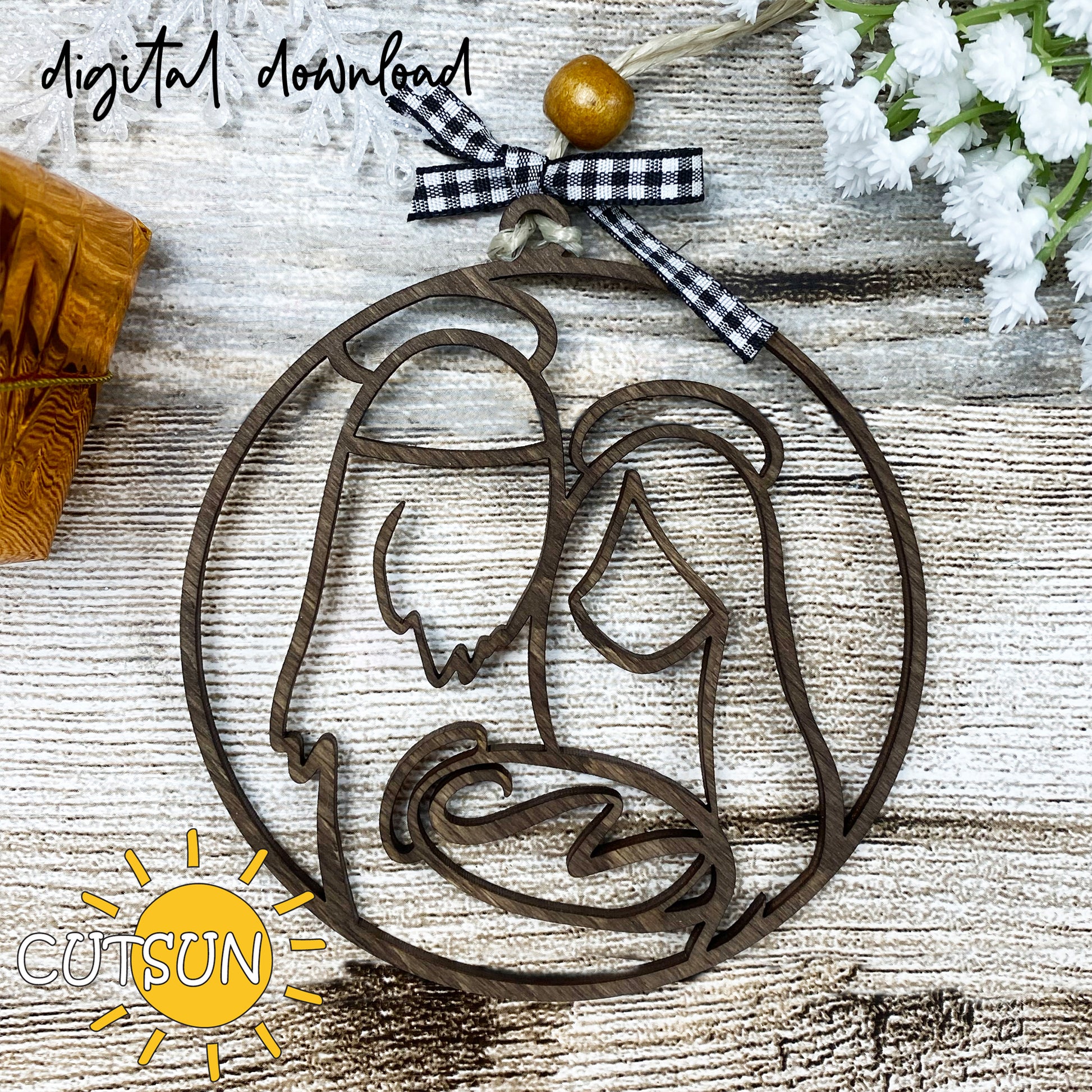 A circular brown Christmas ornament with a nativity scene design, placed on a wooden surface with a checkered ribbon at the top, and digital download text overlayed.