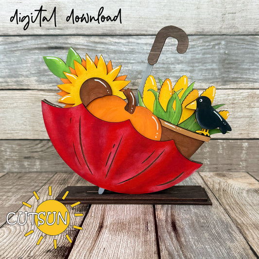 A digital download illustration of a fall-themed scene with an upside down umbrella, layered pumpkins, corn, sunflowers, and a crow, intended for laser cutting.