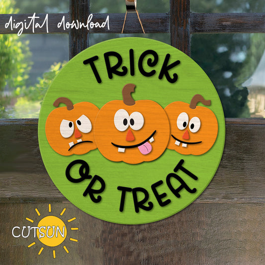 A digital image showing a round door hanger with a green background, featuring three cartoon pumpkins with facial expressions and the text 'TRICK OR TREAT'.