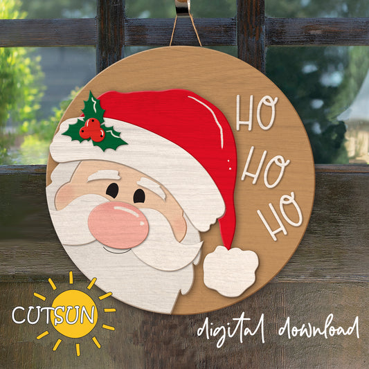 Round Christmas-themed door hanger featuring a smiling Santa Claus with 'Ho Ho Ho' text, decorated with holly and berries, in a red hat and white beard, hanging against a fence.