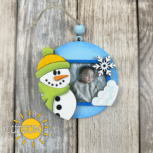 Laser-cut snowman photo ornament SVG with layered design, featuring a winter hat, scarf, snowflake, and a photo slot for 2x2 inch pictures.