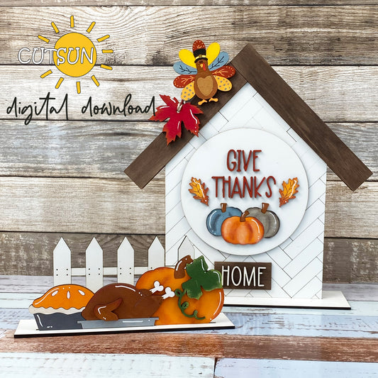 Thanksgiving themed decoration with a digital download link. The image shows a laser cut file design featuring a house, fence, pumpkins, a turkey, and the text 'Give thanks'.