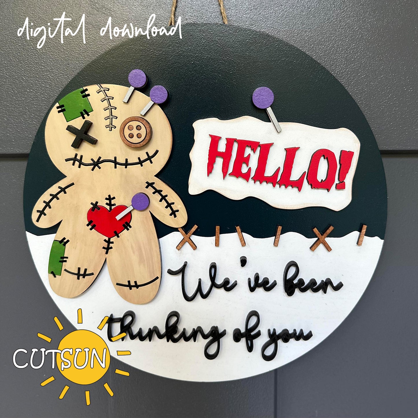 A digital download image of a Voodoo doll door hanger with the text 'Hello! We've been thinking of you.' and decorative elements in black, white, and green colors.