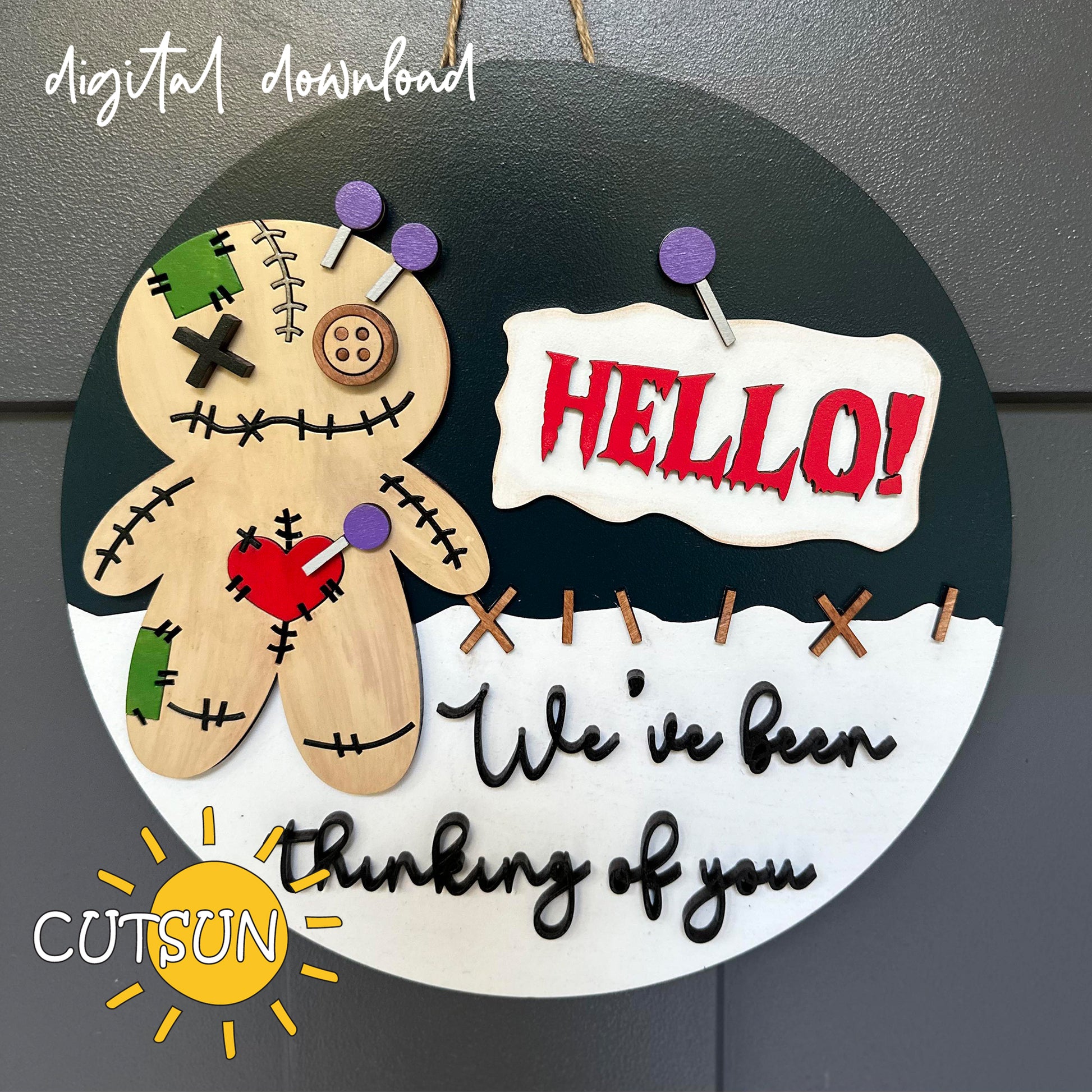 A digital download image of a Voodoo doll door hanger with the text 'Hello! We've been thinking of you.' and decorative elements in black, white, and green colors.