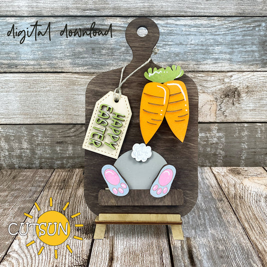Digital download for a faux cutting board shelf sitter with Easter decor featuring two carrots, a bunny but and a tag withthe text 'Happy Easter'.