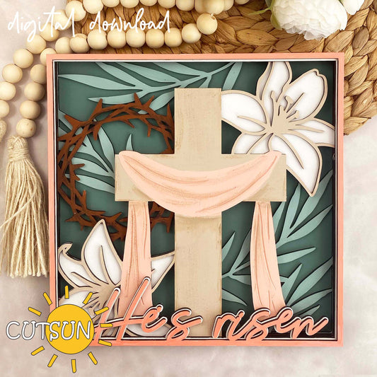 Digital download for an Easter shadow box featuring a cross with a mantle, a lillies, palm leaves, crown with torn and the text 'He's risen'.