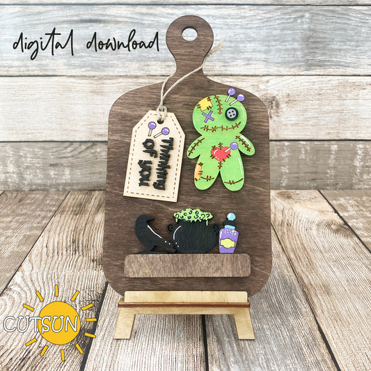 A digital download image showing a wooden cutting board decorated with a Voodoo doll, a raven, a cauldron, a potion bottle, and a tag with the words 'Thinking of you'.