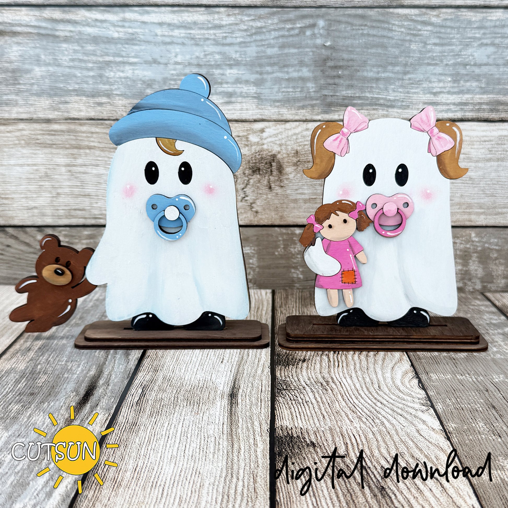 Two cute layered ghost shelf sitters with pacifiers, rosy cheeks and tiny shoes, one holding a teddy bear and the other holding a rag doll, displayed on rustic wooden stands.
