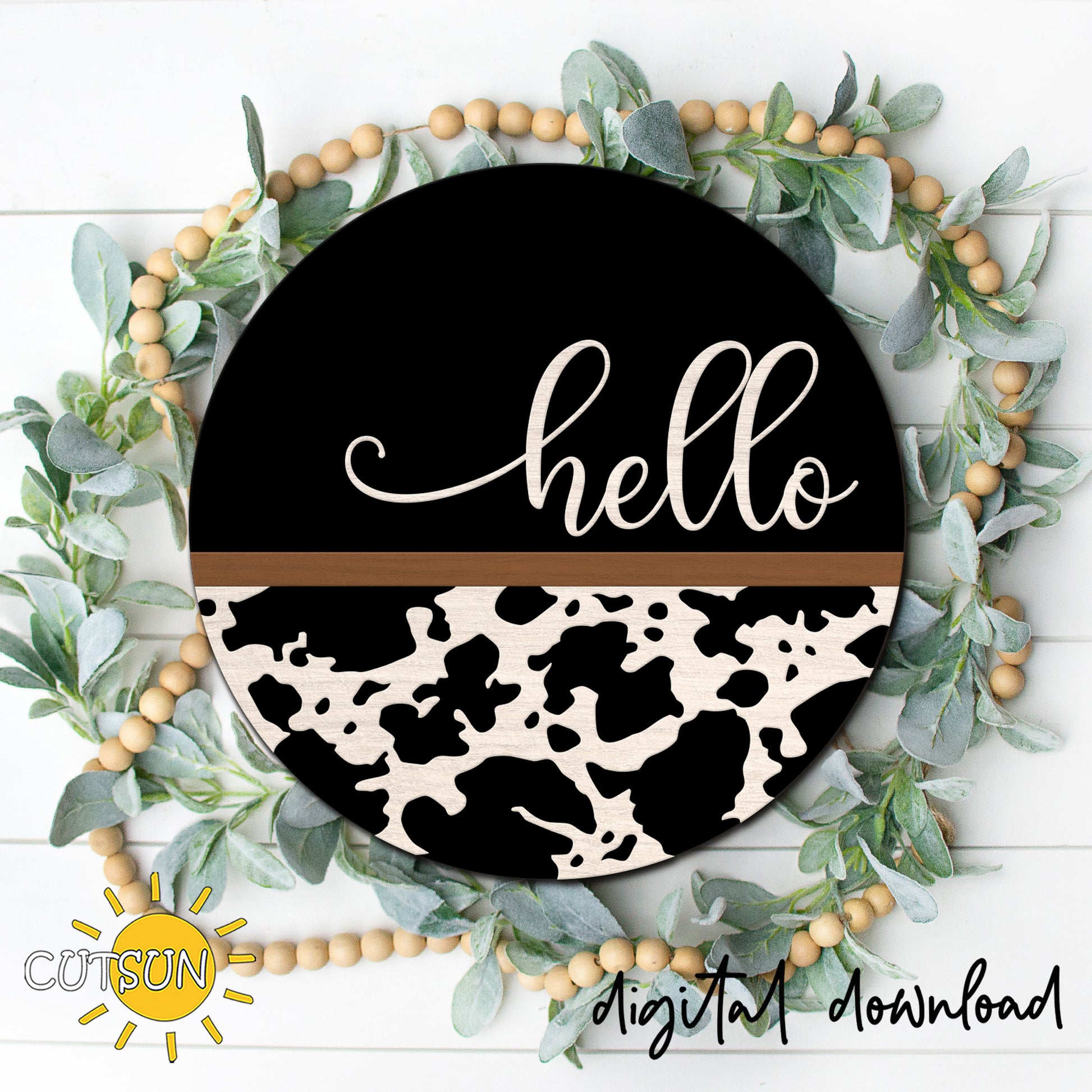Round cow print hello door hanger with black background, white layered script, and western farmhouse style displayed on a front door.