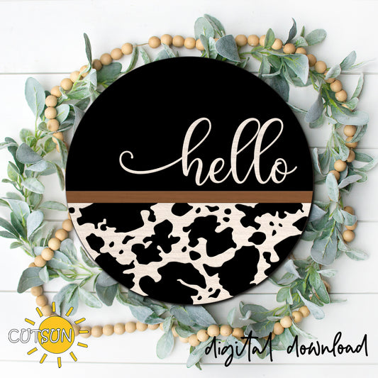 Round cow print hello door hanger with black background, white layered script, and western farmhouse style displayed on a front door.