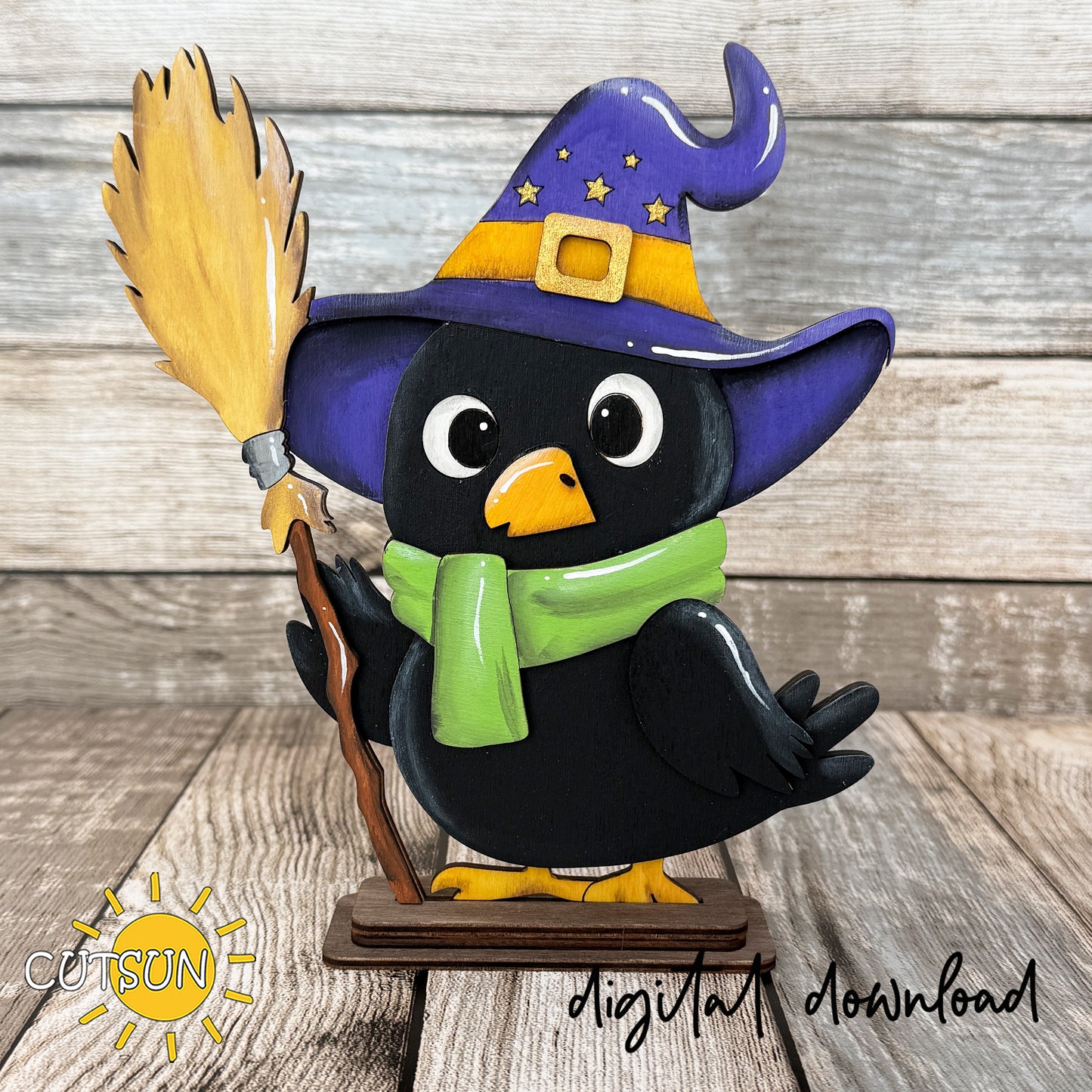 Layered Halloween crow shelf sitter SVG featuring a cute black crow wearing a purple witch hat, green scarf, and holding a broomstick, designed as a freestanding laser cut decoration.