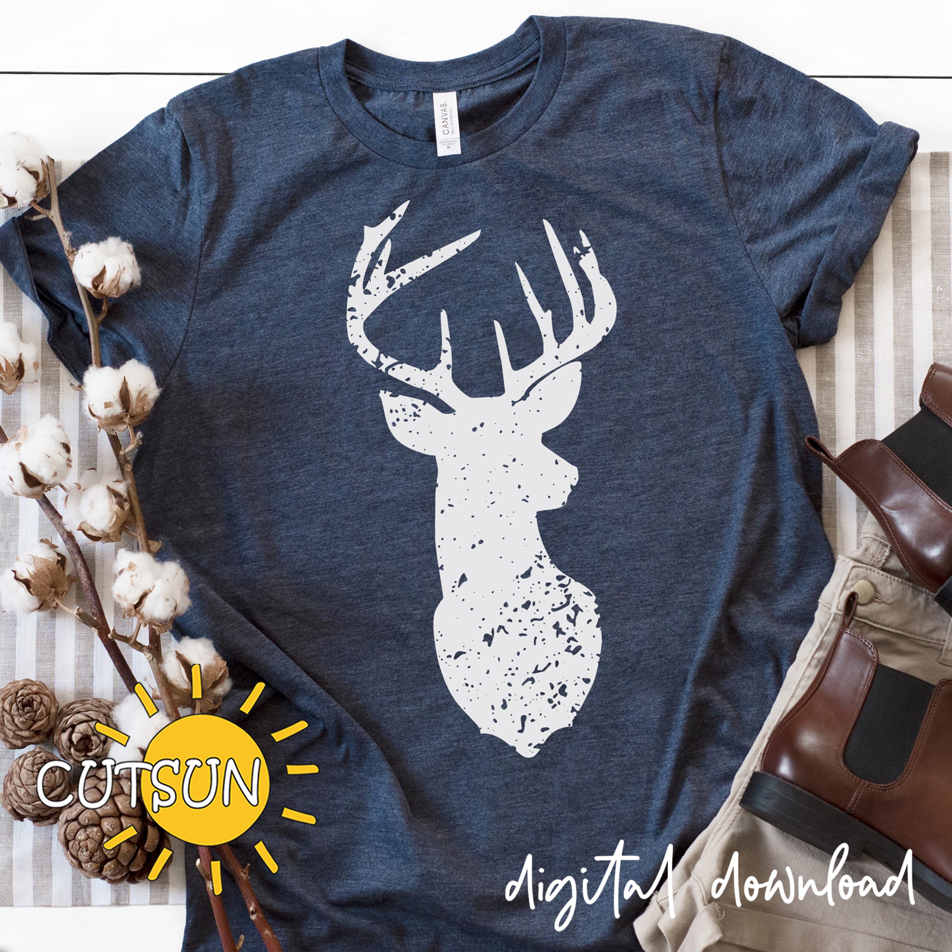 Navy blue t-shirt with white deer head design on a wooden surface with cotton and boots.