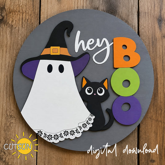 Layered Halloween round door hanger featuring a cute ghost in a witch hat, black cat, colorful BOO lettering, and Hey Boo script on a gray wooden background.