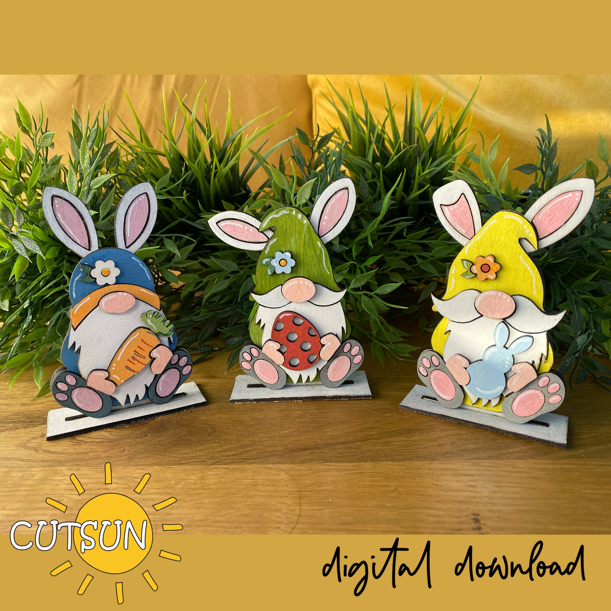 Three colorful gnome figurines with bunny ears on a wooden surface with greenery in the background, branded 'CUTSUN'.