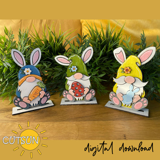 Three colorful gnome figurines with bunny ears on a wooden surface with greenery in the background, branded 'CUTSUN'.