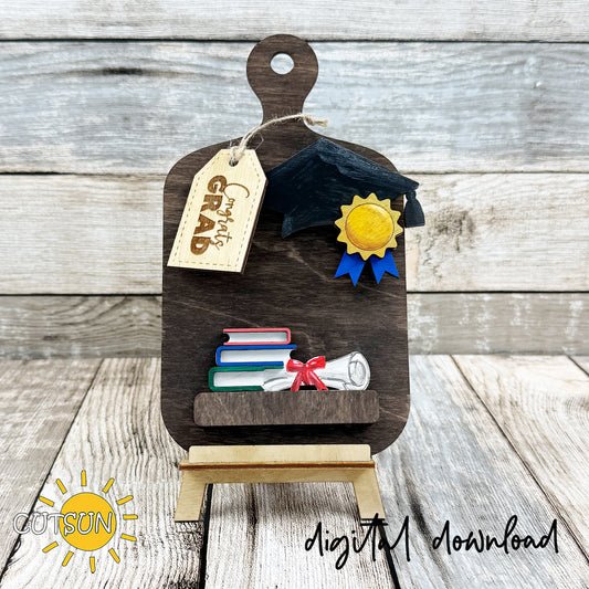 Graduation-themed wooden stand with decorative elements on a wooden surface, featuring the brand 'CutsieSun'.