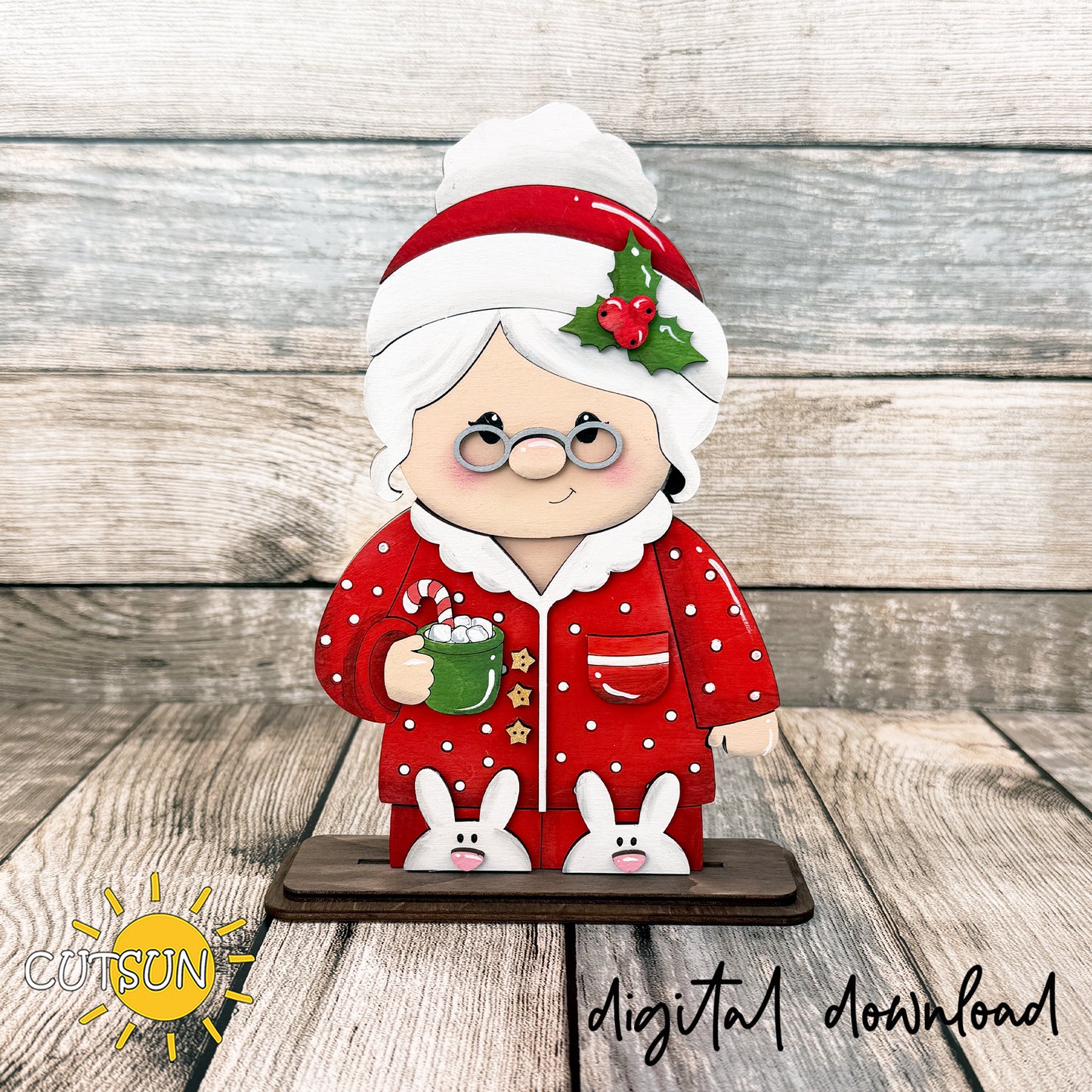 Layered wooden Mrs. Claus shelf sitter wearing red Christmas pajamas and bunny slippers while holding a green mug of hot cocoa.