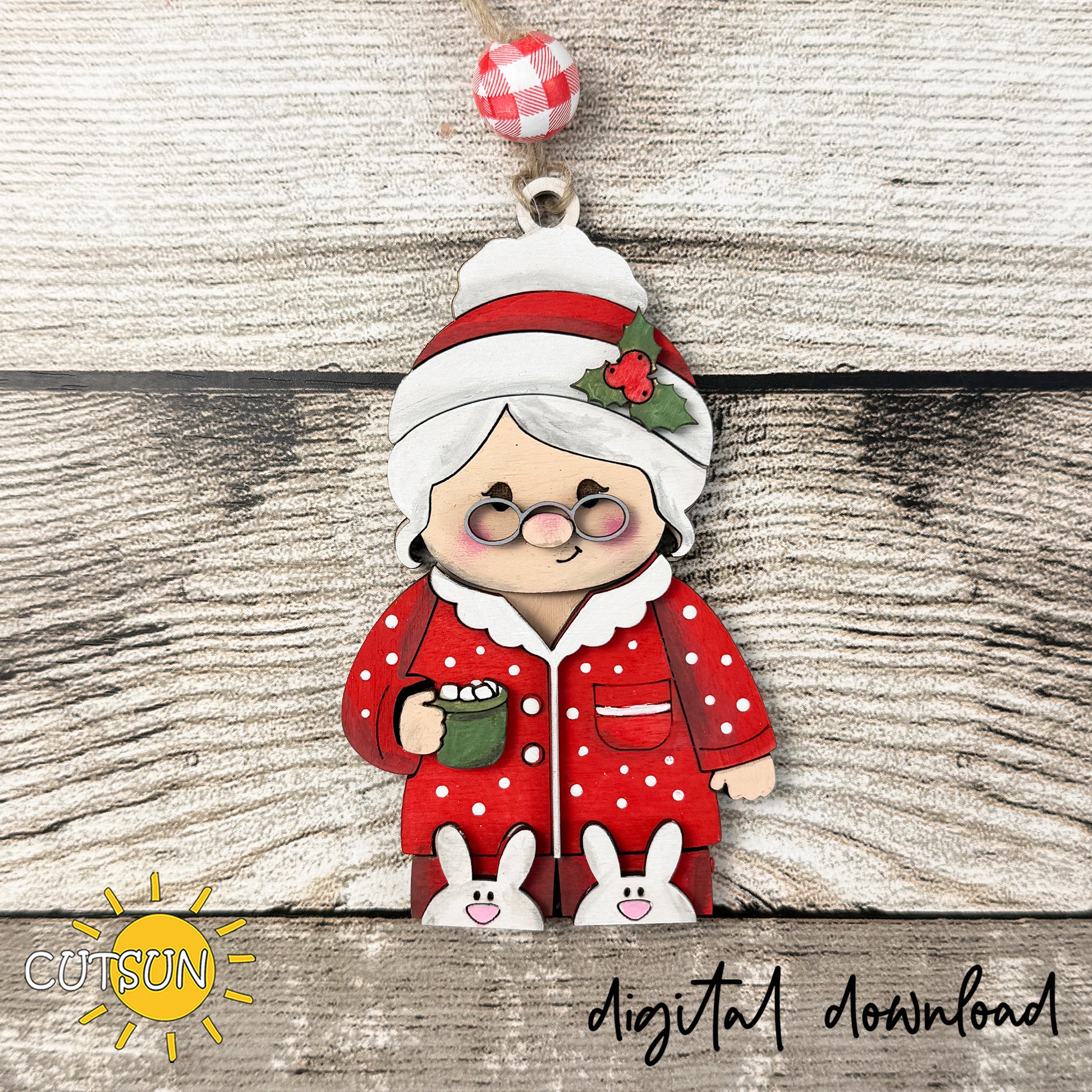 Layered wooden Mrs. Claus Christmas ornament wearing red polka-dot pajamas and bunny slippers while holding a green mug of hot cocoa.