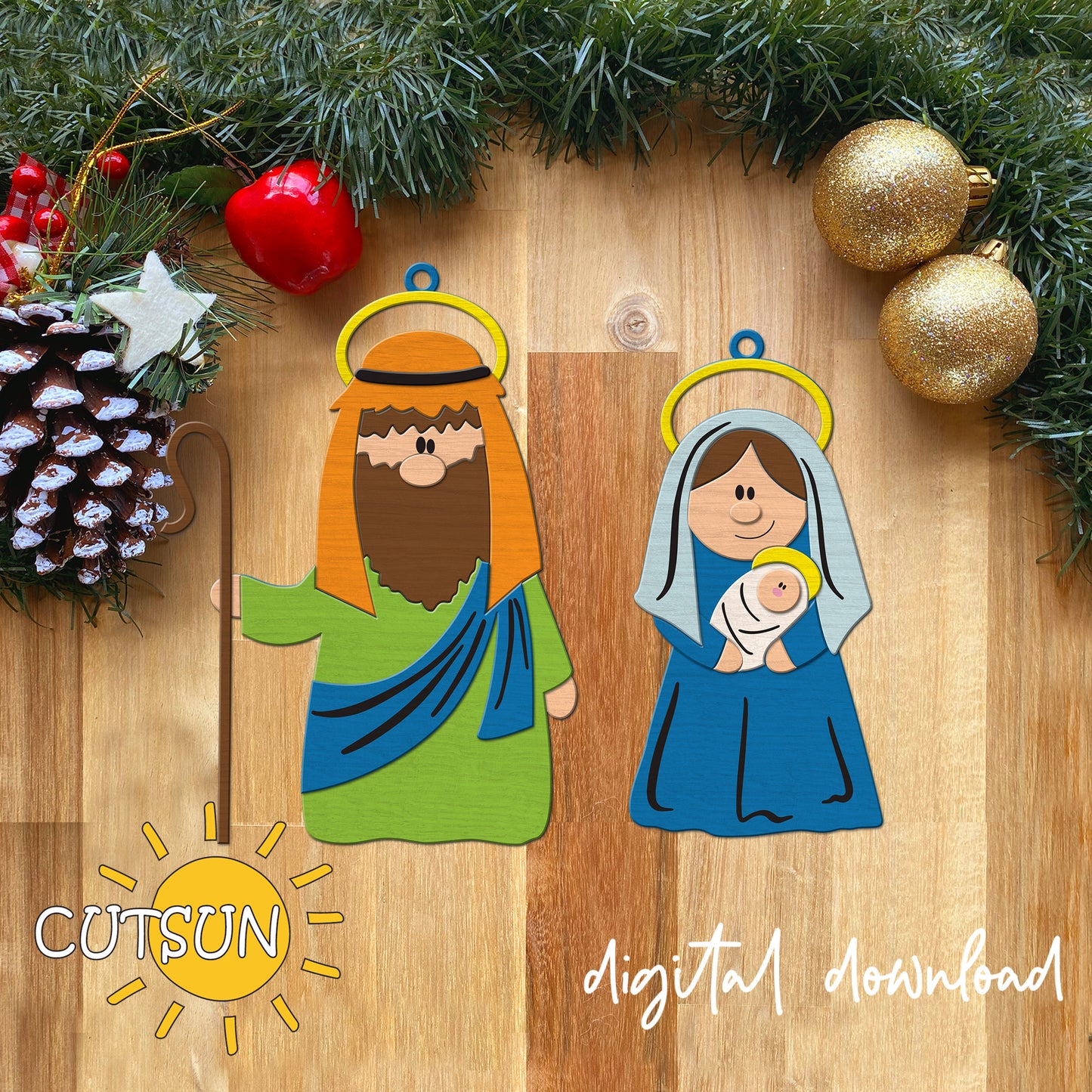 Decorative cutouts of a man and woman holding a baby on a wooden surface with Christmas decorations.