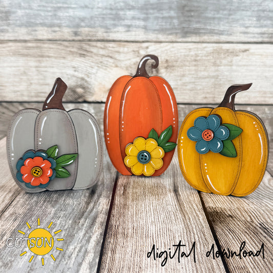 Set of three layered wooden pumpkin shelf sitters in gray, orange and mustard yellow, featuring stitched details, button-centered flowers and rustic farmhouse fall colors.