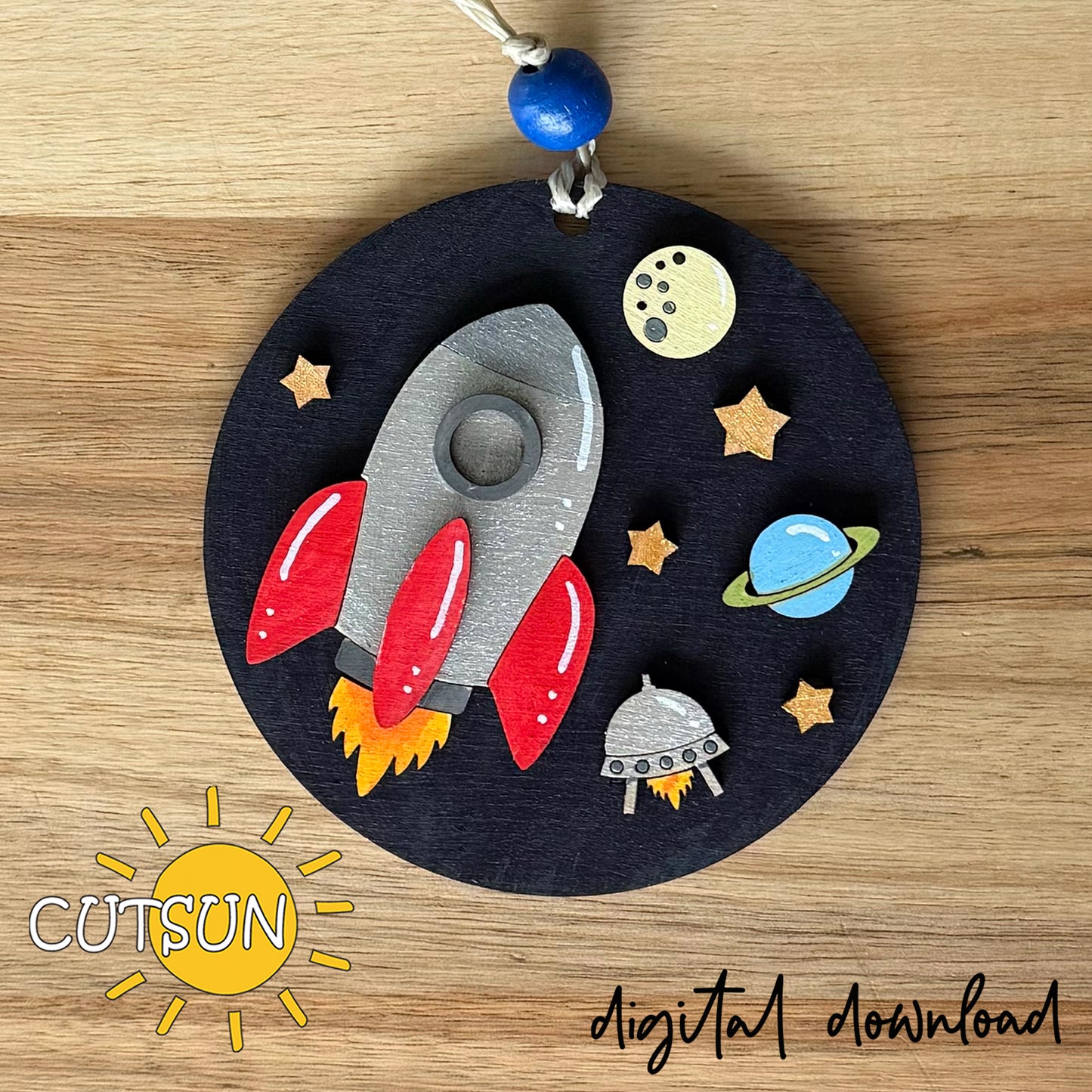 Laser cut Rocket and Planets ornament SVG with UFO, stars, and moon on dark round base.
