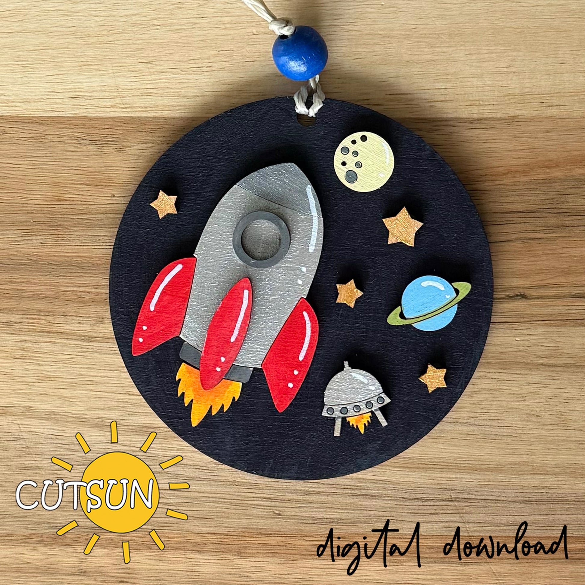 Laser cut Rocket and Planets ornament SVG with UFO, stars, and moon on dark round base.