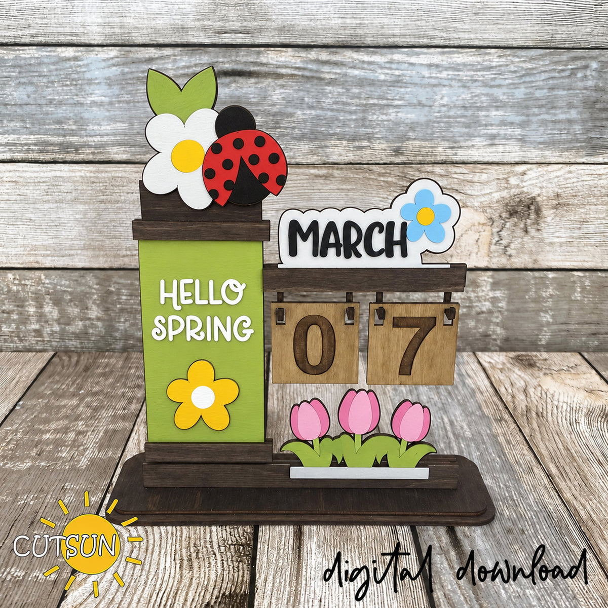 Wooden desktop calendar with March flower sign, ladybug topper, green Hello Spring panel, and pink tulip decoration.