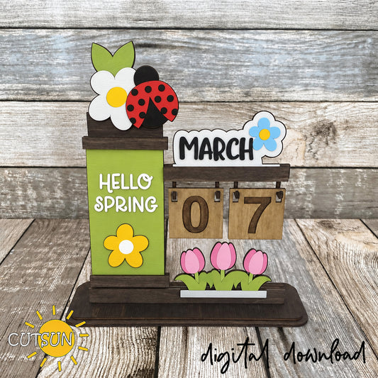 Wooden desktop calendar with March flower sign, ladybug topper, green Hello Spring panel, and pink tulip decoration.