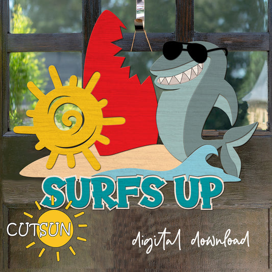 Layered wooden door hanger with a smiling shark in sunglasses, red surfboard, yellow sun, and the phrase “Surf’s Up” in bold letters.