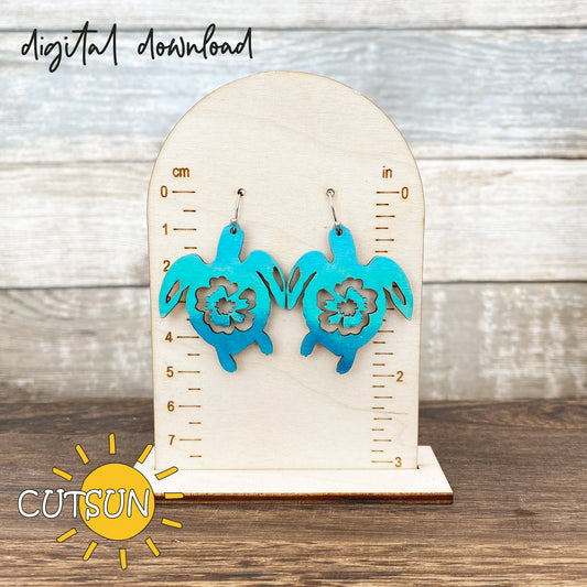 Pair of turquoise sea turtle earrings displayed on a wooden measurement stand, perfect for laser-cut jewelry crafts.